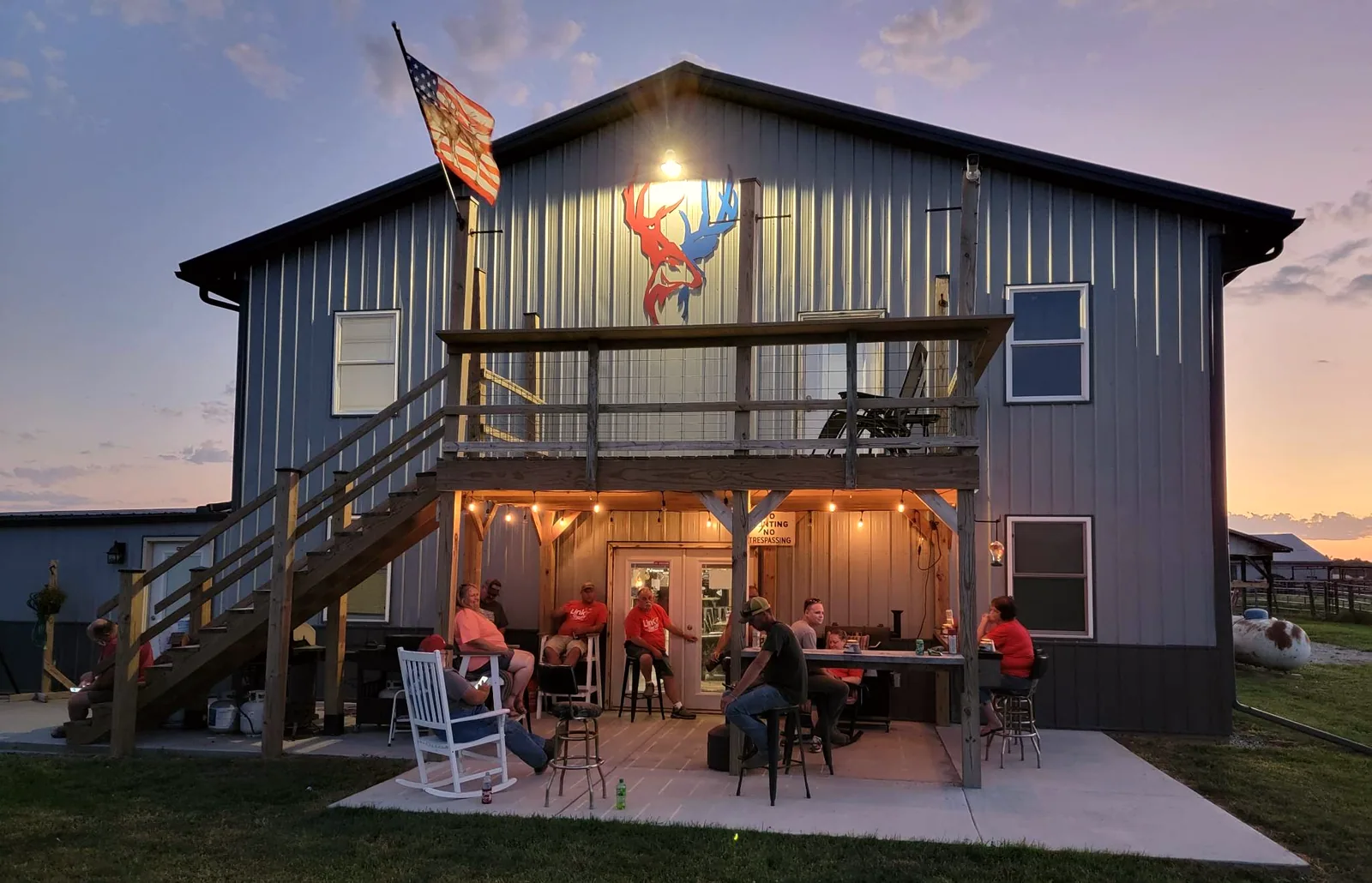 The Bigger Bucks Outfitters lodge lit at dusk in Media Illinois with hunters on the deck